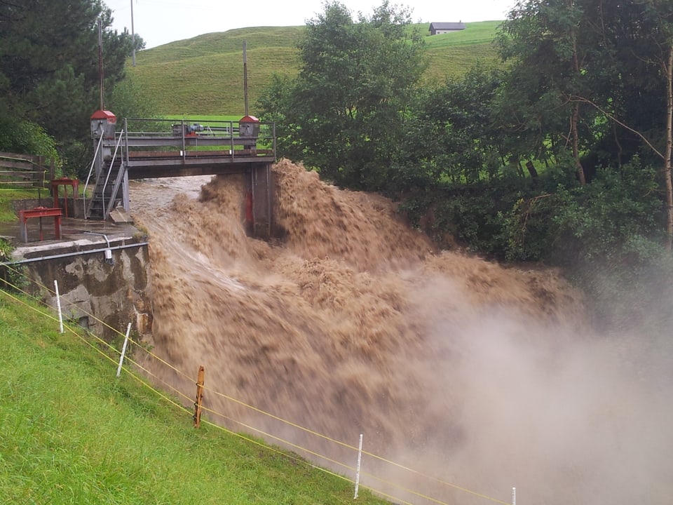 Der Fotograf steht unterhalb einer Brücke. Der Bach ist nun ein reissender, brauner Fluss. Die Brücke ist zu klein um das ganze Wasser zu kanalisieren. Die Brückenpfeiler werden umspült.