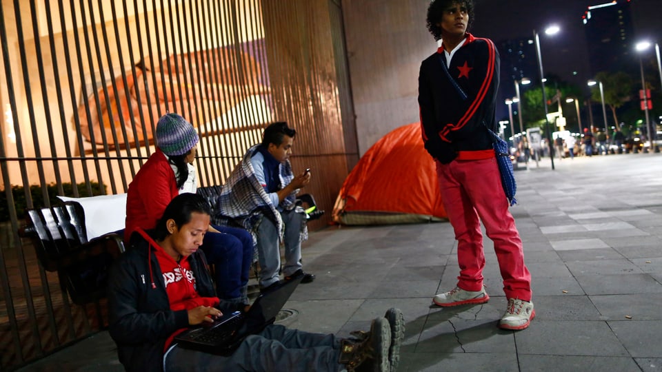 Drei Migranten aus Zentralamerika sitzen am Boden vor einem vergitterten Fenster, einer steht