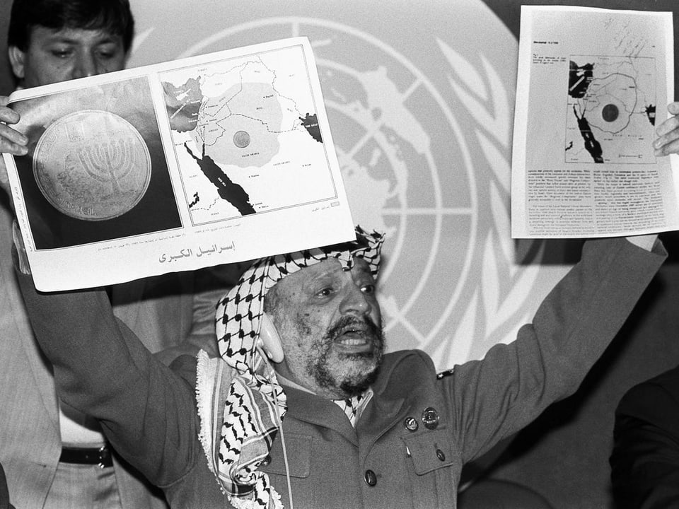 Arafat hält zwei Karten in die Höhe, die das Gebiet in Nahost abbilden