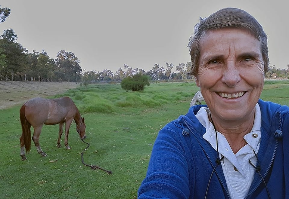 Selfie einer Frau mit einem fressenden Pferd im Hintergrund.