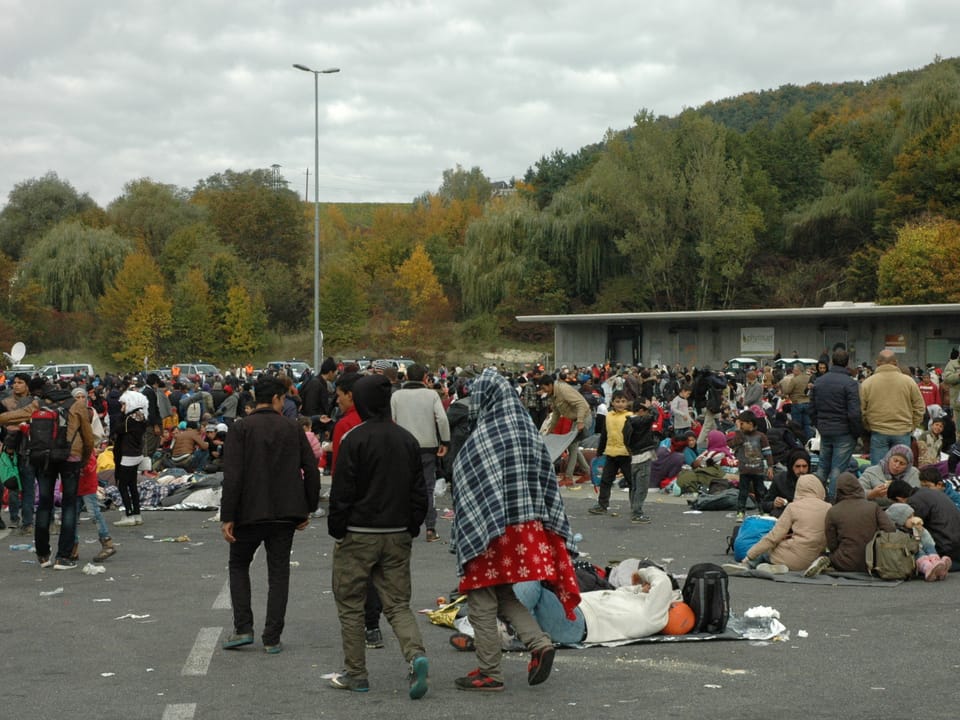 Viele Flüchtlinge sitzen am Boden oder laufen auf einem grossen Steinplatz herum.