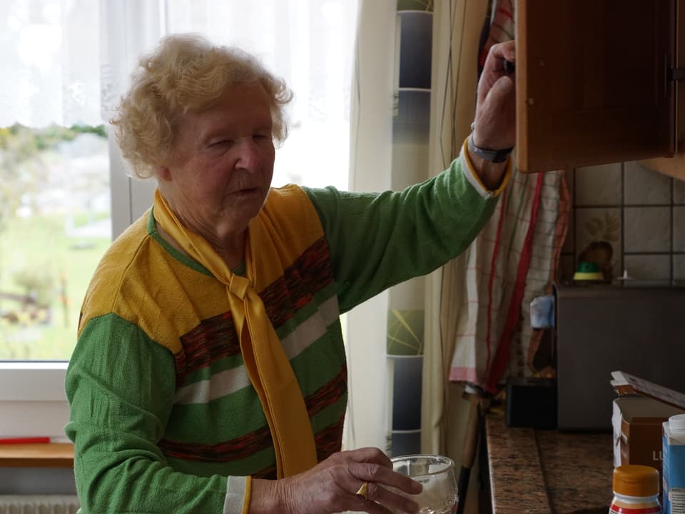 Die Seniorin nimmt sich ein Glas aus dem Küchenschrank.