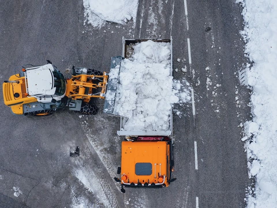 Ein Bagger schaufelt Schnee in einen LKW