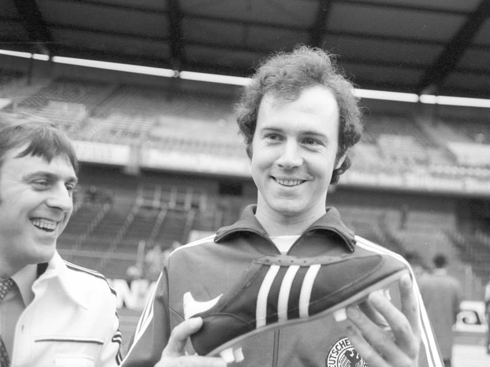 Der junge Franz Beckenbauer hält einen Adidas-Fussballschuh in die Kamera.