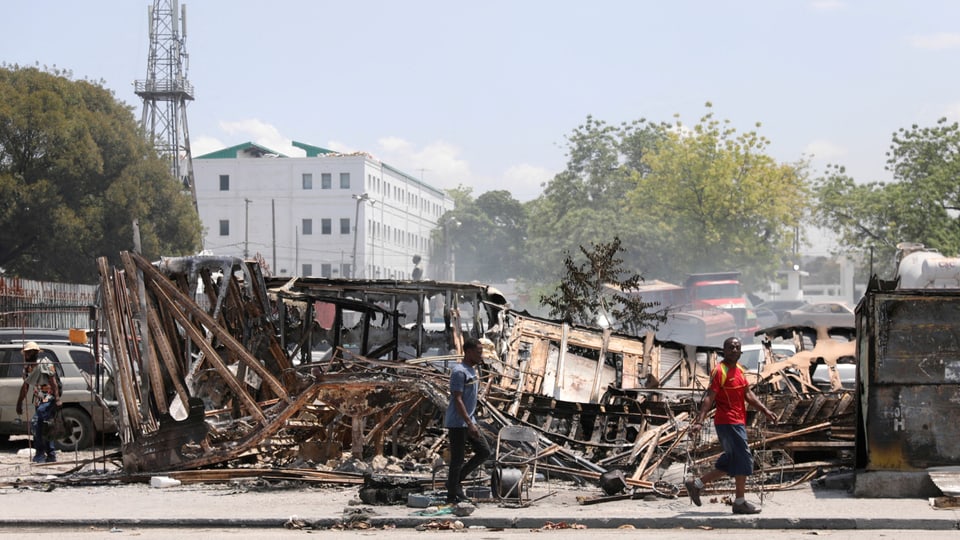 Verbrannte Fahrzeuge und zwei unverletzte Personen auf einer zerstörten Strasse in Port-au-Prince..