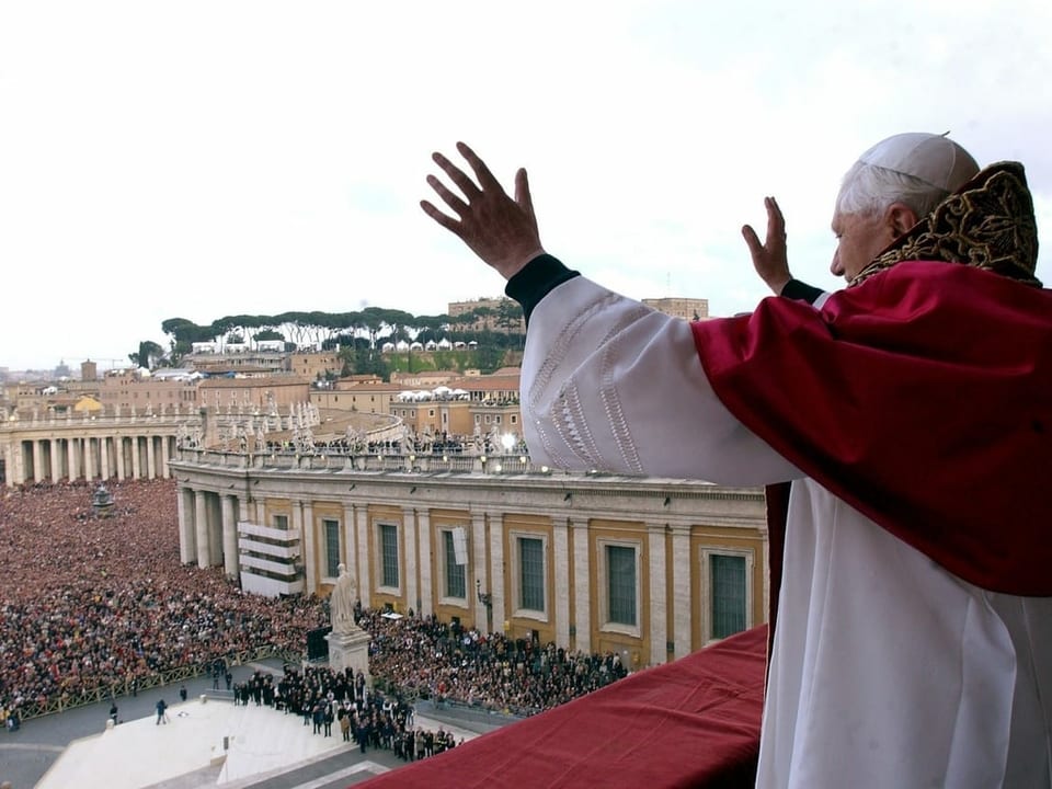 Der Papst steht auf dem Balkon und winkt der Menge auf dem Petersplatz.
