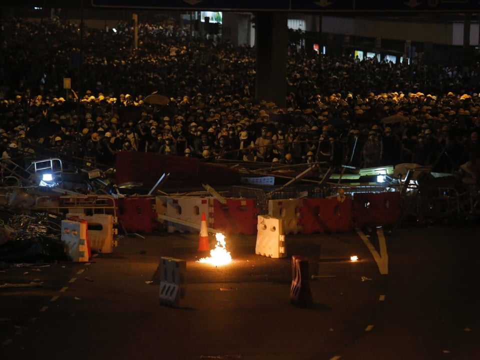 Barrikade im Dunkeln, dahinter Menschenmassen, davor eine brennende Benzinbombe