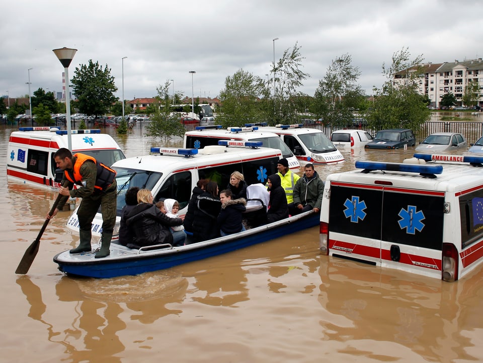 Ein Mann steuert ein Boot zwischen überschwemmten Ambulanzen hindurch.