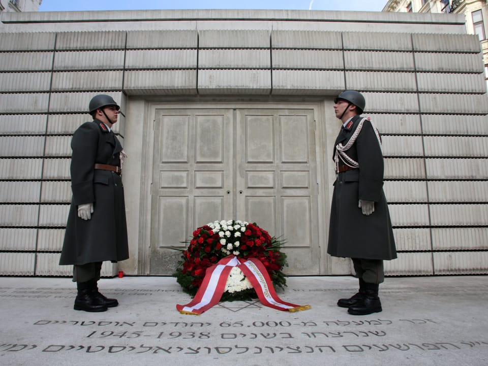 Zwei Soldaten stehen vor einem grossen grauen Denkmal.