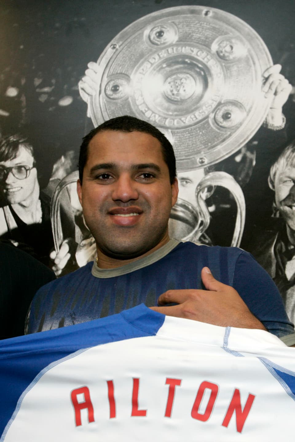 Aílton Gonçalves da Silva hält seuin T-Shirt und lächelt in die Kamera