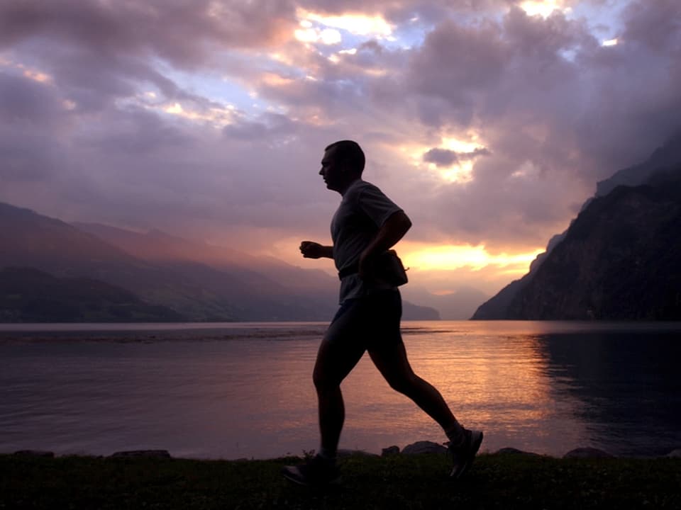 Dunkler Umriss einer joggenden Person, im Hintergrund violette Abendstimmung mit vielen Wolken, See und Berge.
