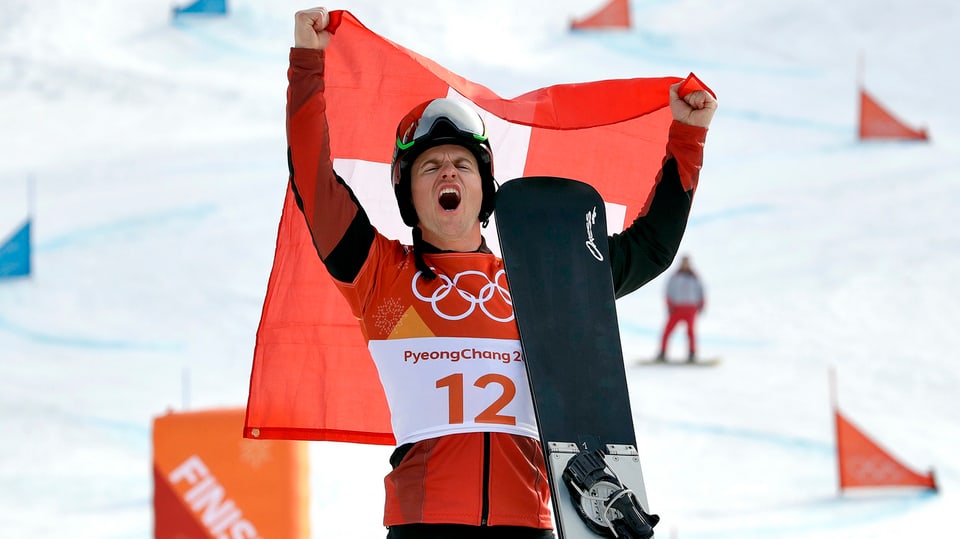 Mann hälft Schweizer Fahne in die Höhe und Snowboard in der Hand