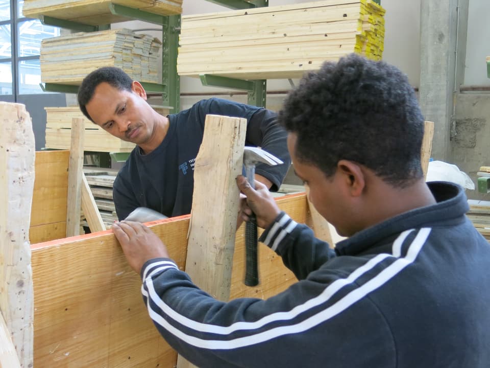 Zwei Männer halten ein Holzbrett.