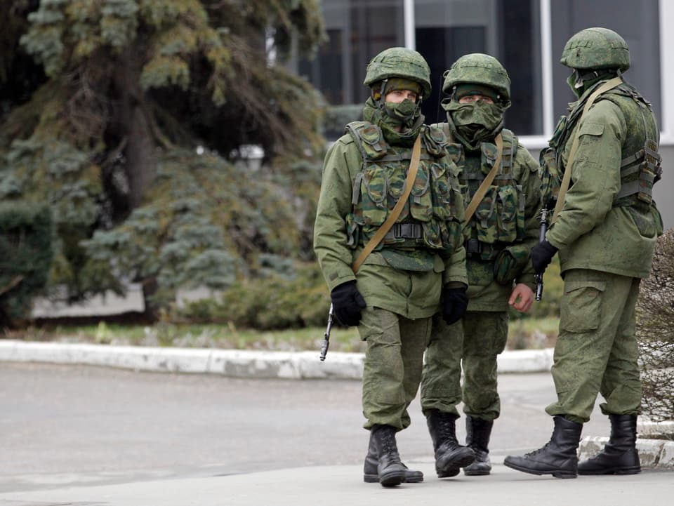 Drei unbekannte bewaffnete Männer patroullieren vor dem internationalen Flughafen in Simferopol auf der Krim. Sie tragen militärische Kleidung. 