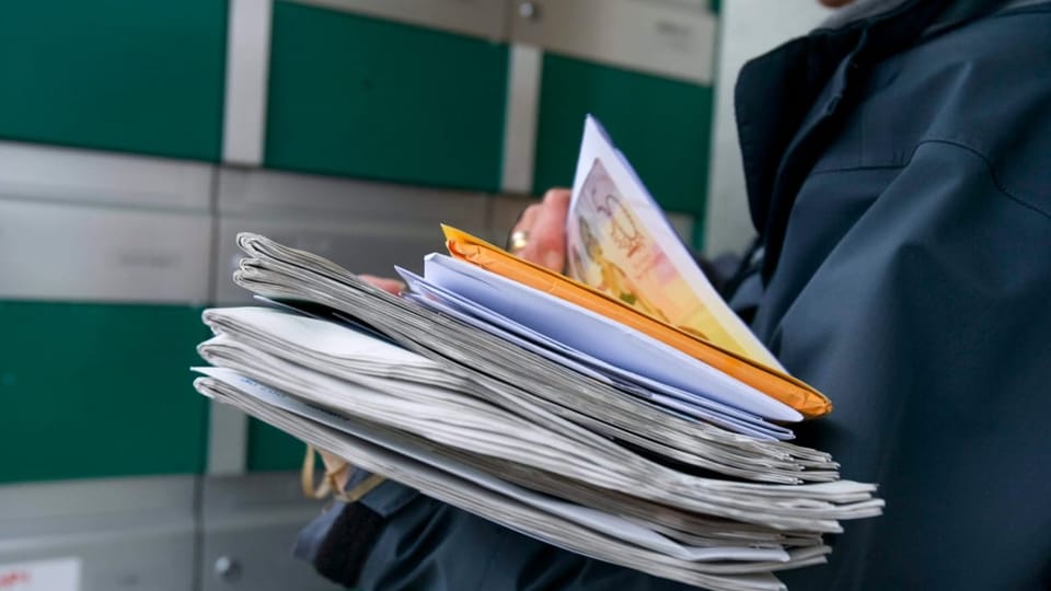 Pöstlerin wirft Briefe und Zeitungen in die Briefkästen eines Mehrfamilienhauses
