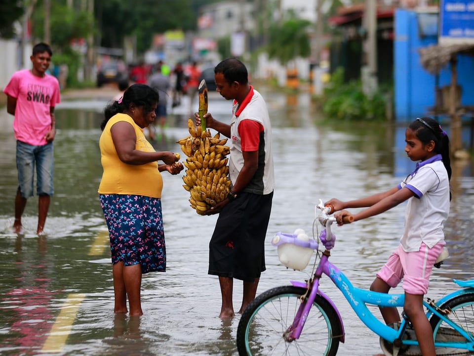 Eine Person verkauft Bananen in einer überschwemmten Strasse.