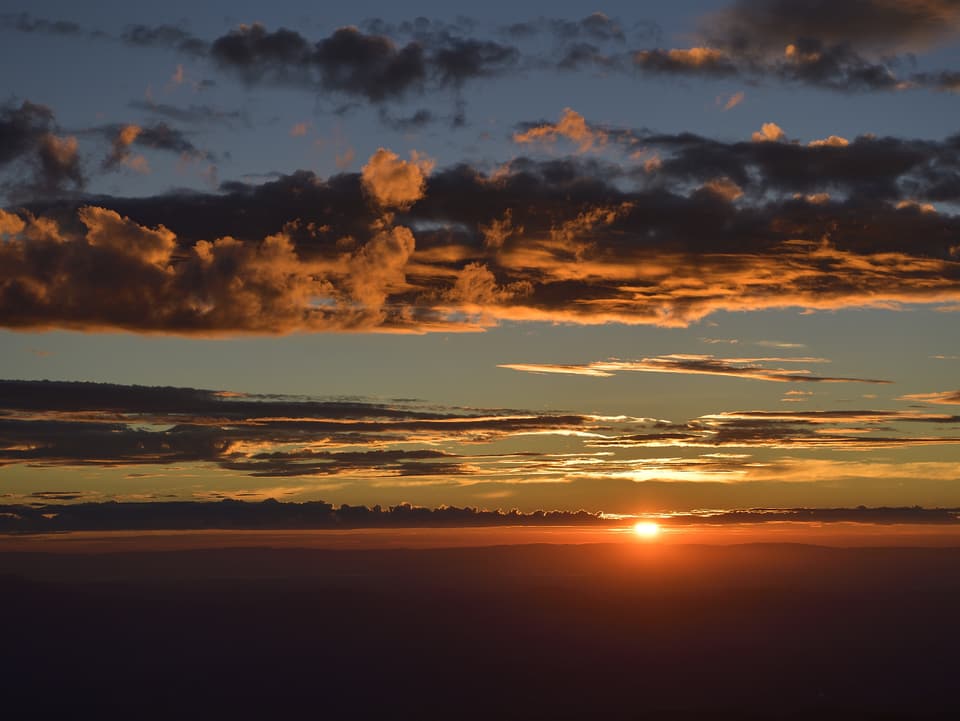 Feuerrot geht die Sonne am Horizont unter. Die Wolkenfelder werden in ein warmes, rötliches Licht getaucht.
