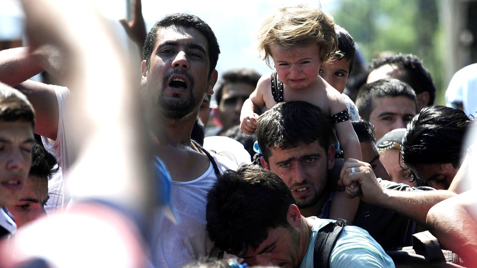 Eine Menschenmenge von Flüchtenden an der Grenze zwischen Mazedonien und Serbien. Ein kleines Mädchen sitzt auf den Schultern eines zerknirscht dreinschauenden Mannes und weint.