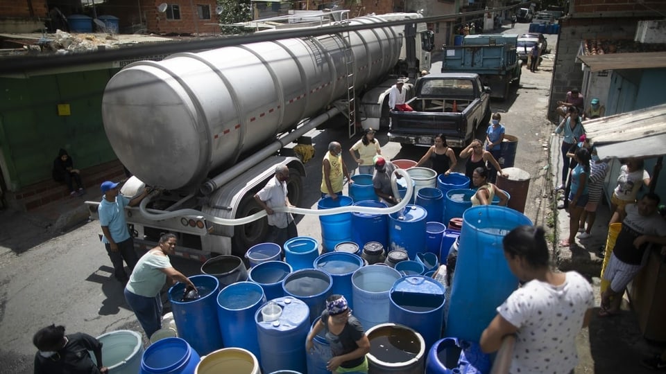 Einwohner von Caracas füllen Trinkwasser aus einem Tanklaster in grosse blaue Fässer.