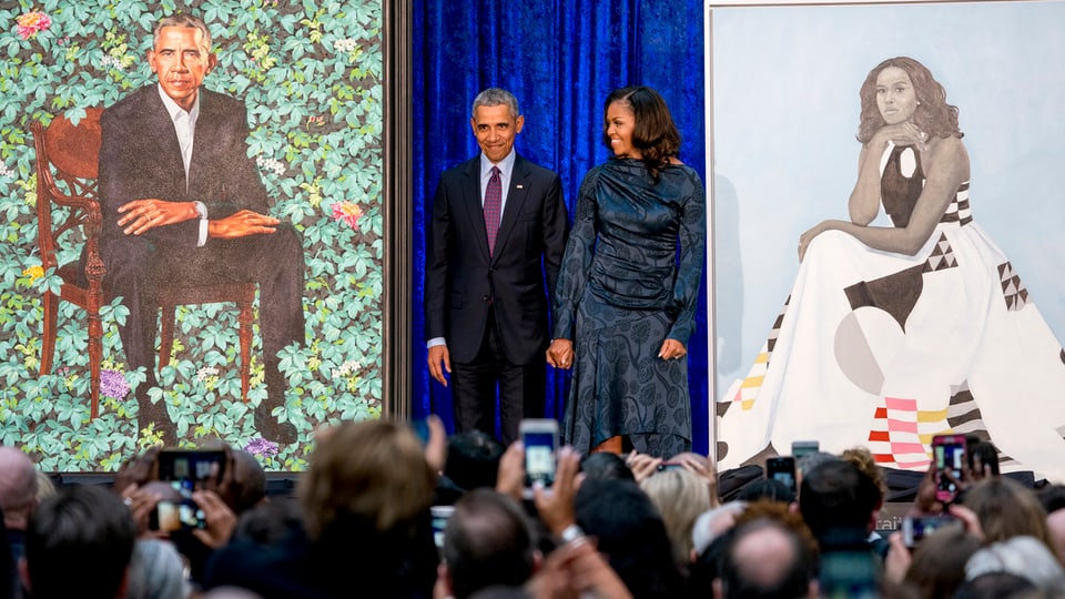 Die Obama stehen neben den Porträts.