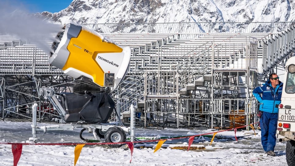 Ein Mann steht neben einer Schneemaschine, dahinter eine leere Tribüne.