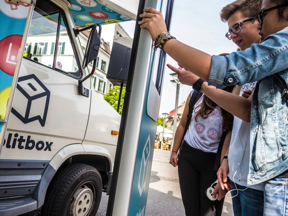 Jugendliche klicken auf einem grossen Smartphone vor dem politbox-Bus.