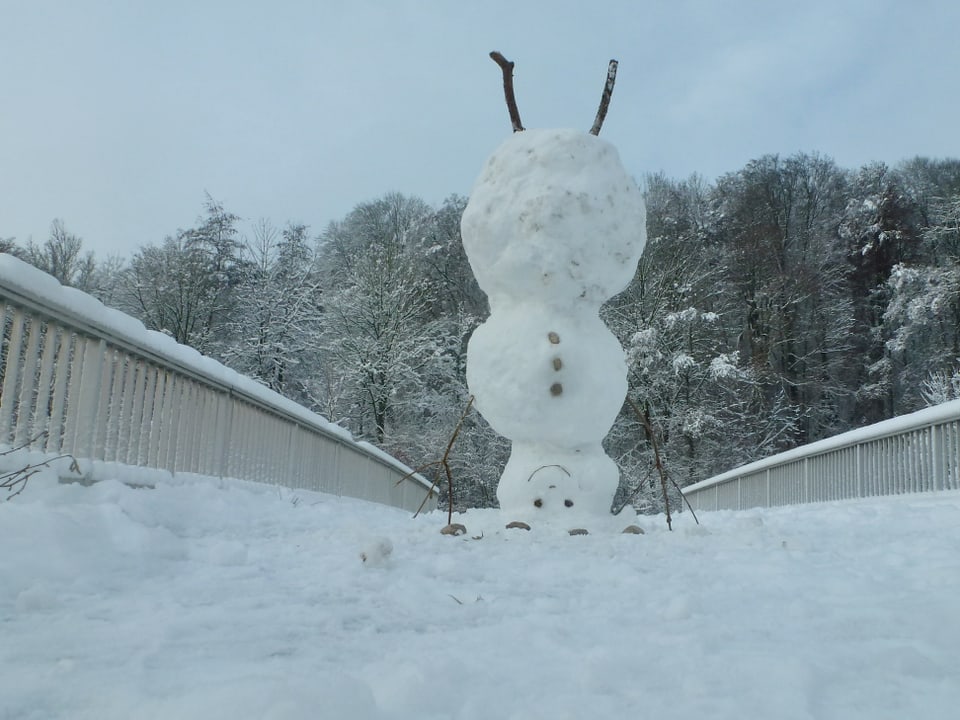 Brücke mit viel Schnee, darauf ist ein Schneemann, er steht auf dem Kopf. 