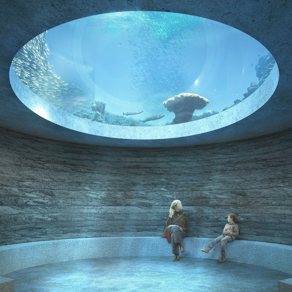 Eine Frau und ein Kind sitzen in einem runden Raum. Über ohrem Kopf öffnet sich die Decke in ein grosses Aquarium. 