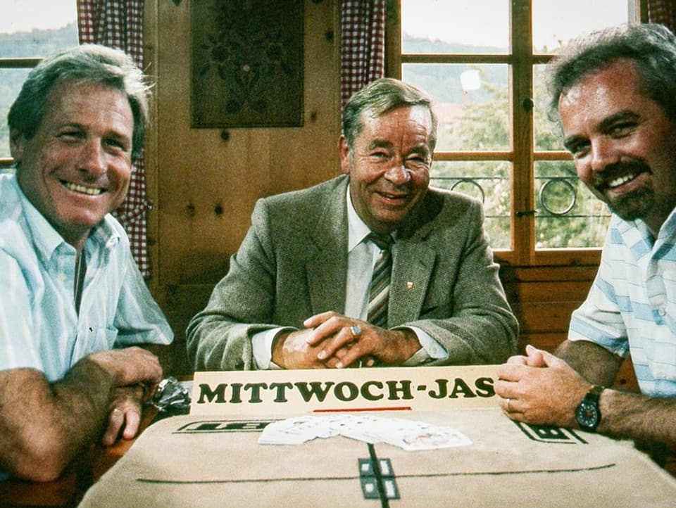 Jürg Randegger, Göpf Egg und Hans Ricklin sitzen am Jasstisch und schauen in die Kamera