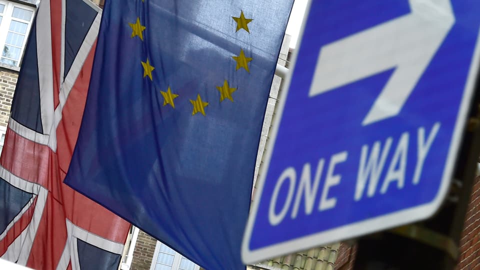 Eine britische Flagge hängt hinter einer EU-Fahne davor ist ein britisches Einbahnstrassenschild zu sehen.