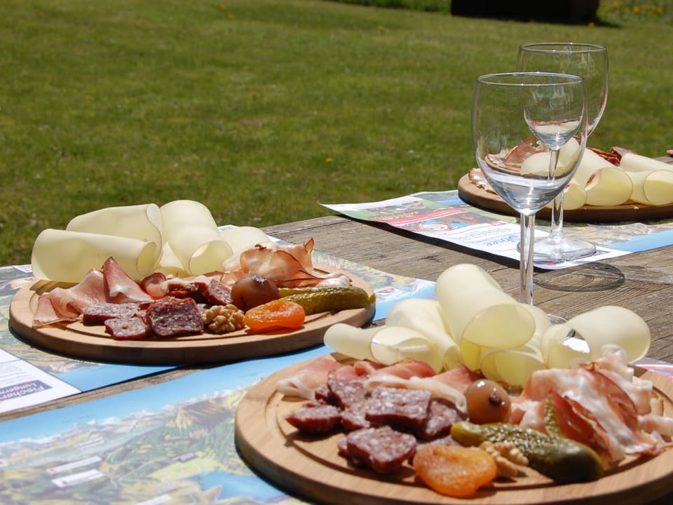 Wurst und Käse auf Holztellern neben Weingläsern.