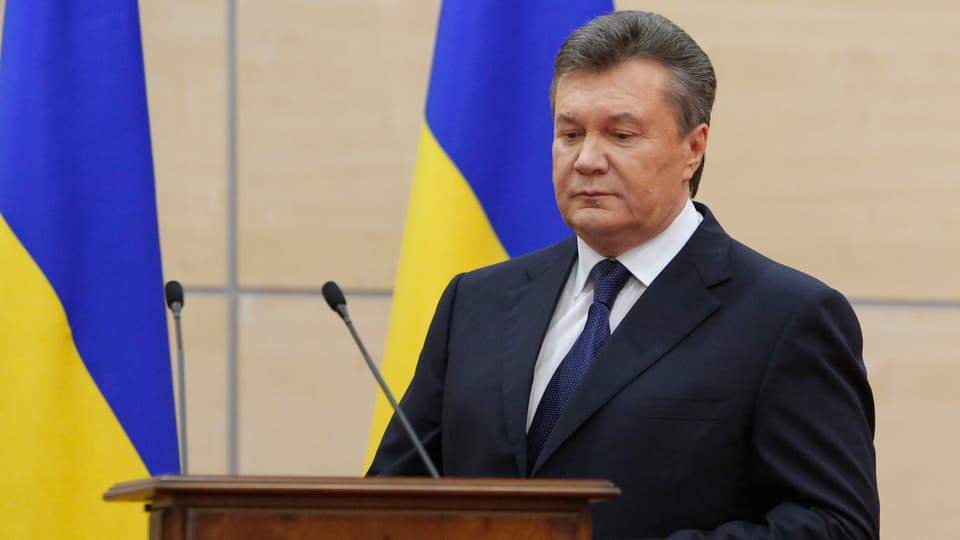 Ex-Präsident der Ukraine, Viktor Janukowtisch, während einer Rede im März 2014. Hinter ihm die ukrainische Flagge in Blau und Gelb. Er selbst blickt nach unten. 