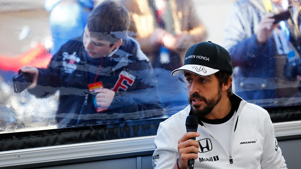 Fernando Alonso gibt ein Interview. Im Hintergrund knipst ein Junge ein Foto des Formel-1-Piloten.