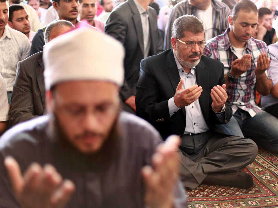 Mursi und weiter Gläubige sitzen auf dem Boden und beten