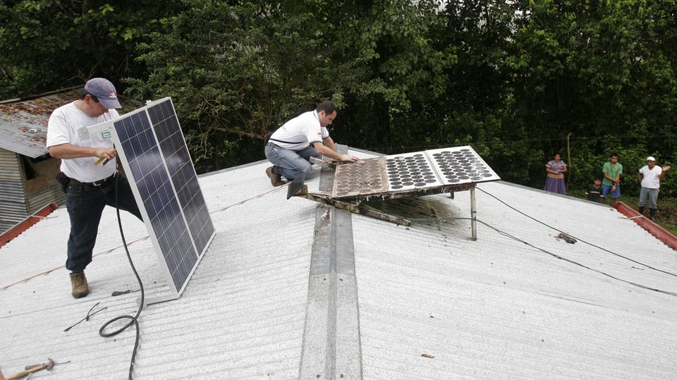 Zwei Männer montieren auf einen Hausdach ein Solarpanel.