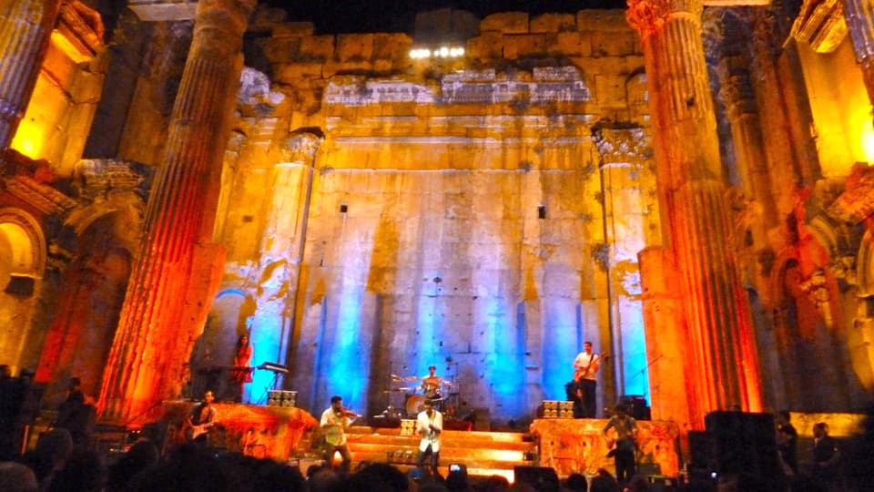 Eine Band spielt in einem antiken Tempel, der farbig beleuchtet ist. 