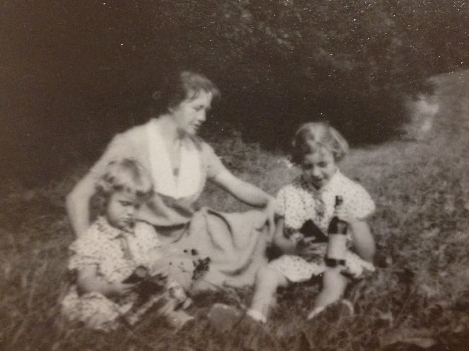 Zwei Mädchen und eine Frau sitzen auf einem Feldweg am Rande einer Wiese.