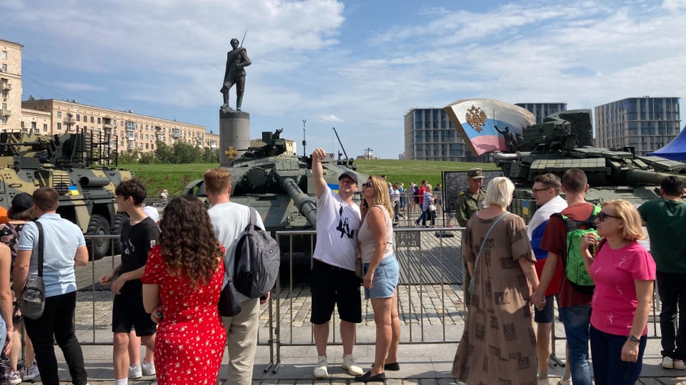 A couple poses in front of a tank