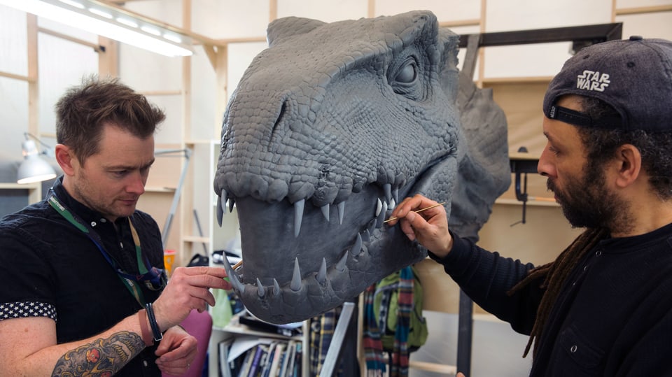 Zwei Männer arbeiten mit feinen Pinseln am einem Modell eines Dinosaurier-Kopf.