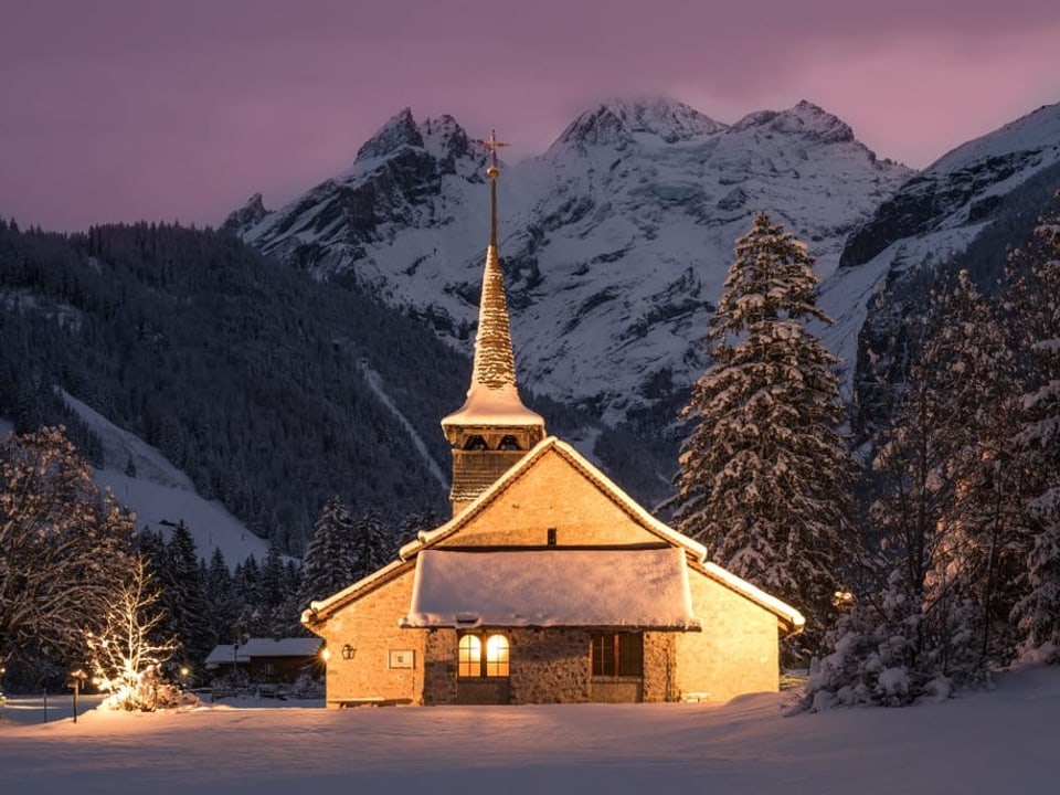 Beleuchtete Kirche in tief verschneitem Tal in der violetten Dämmerung     