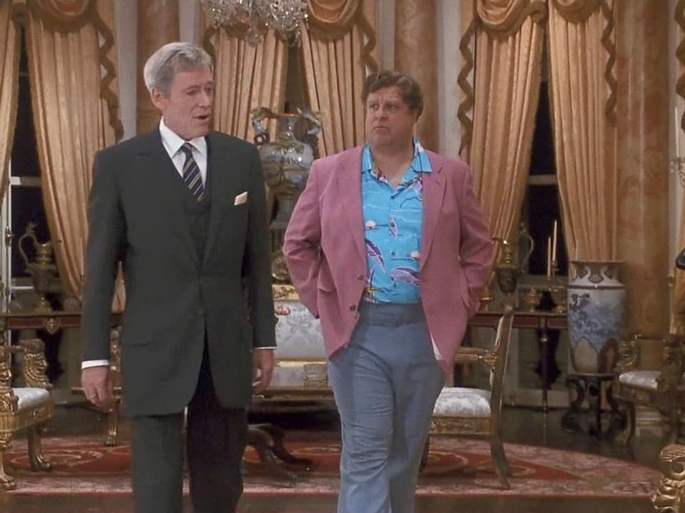 Ein gut gekleideter, älterer englischer Herr steht neben einem Amerikaner in Freizeitkleidung.