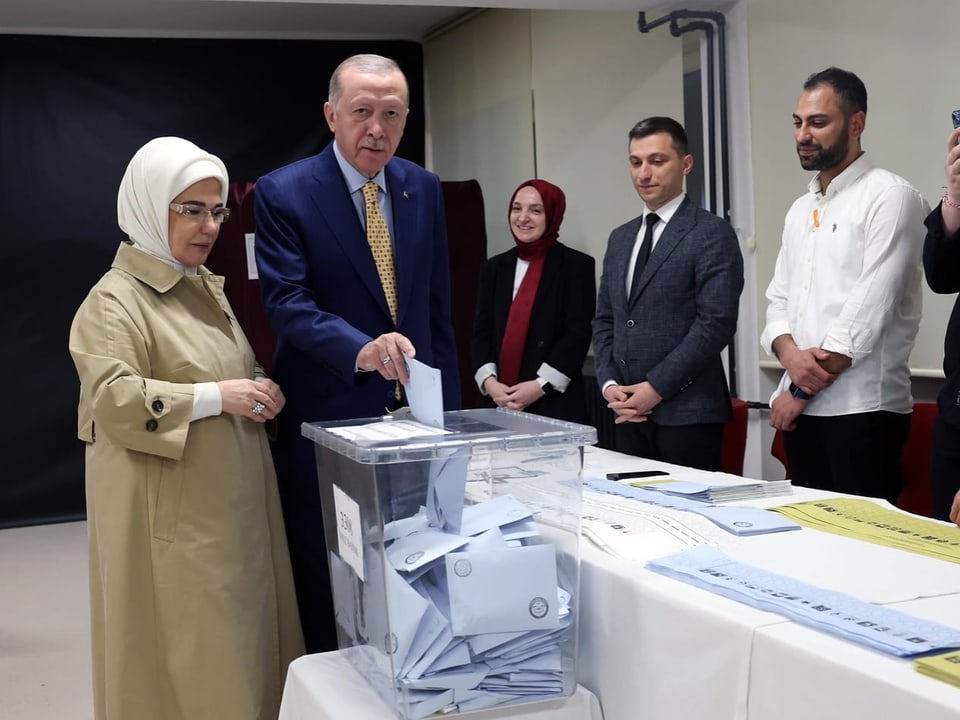 Recep Tayyip Erdogan steht mit seiner Frau in einem Wahllokal und wirft einen Brief in eine Urne.