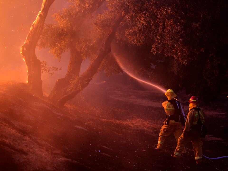 Zwei Feuerwehrmänner versuchen die Flammen zu bekämpfen.