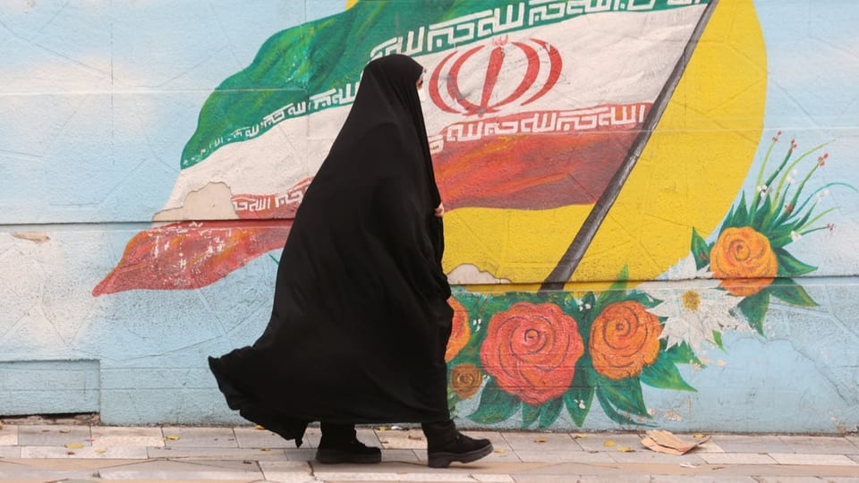Eine komplett verhüllte Frau läuft an einer mit der iranischen Flagge bemalten Wand vorbei.