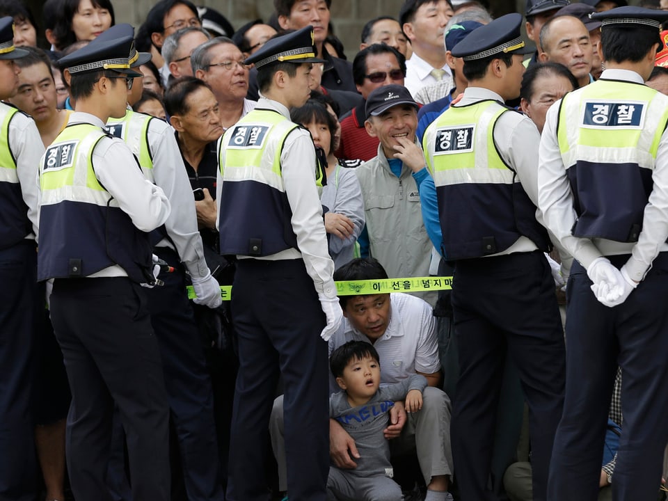Eine Reihe von südkoreanischen Polizisten stellt sich vor die Menge der Schaulustigen, ein kleiner Junge kniet und betrachtet voller Faszination die Parade.