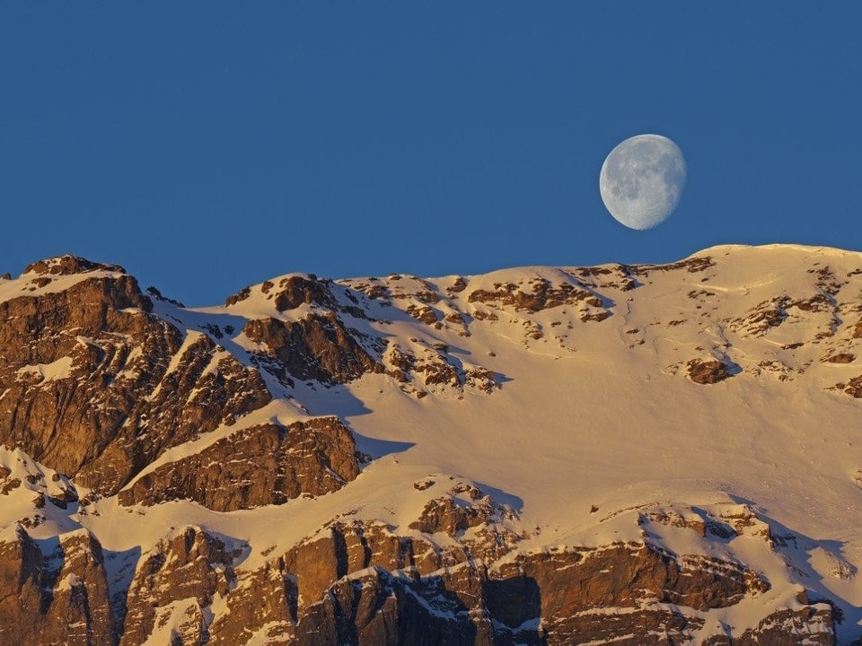 Die Sonne beleuchtet die bereits die verschneiten Hänge des Tschajetugrates. Noch steht aber der Mond und nicht die Sonne über dem Grat.