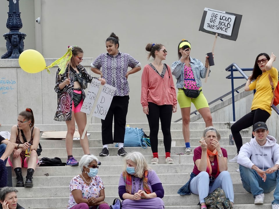 Frauen sitzen oder stehen mit Plakaten auf dem Theaterplatz. 