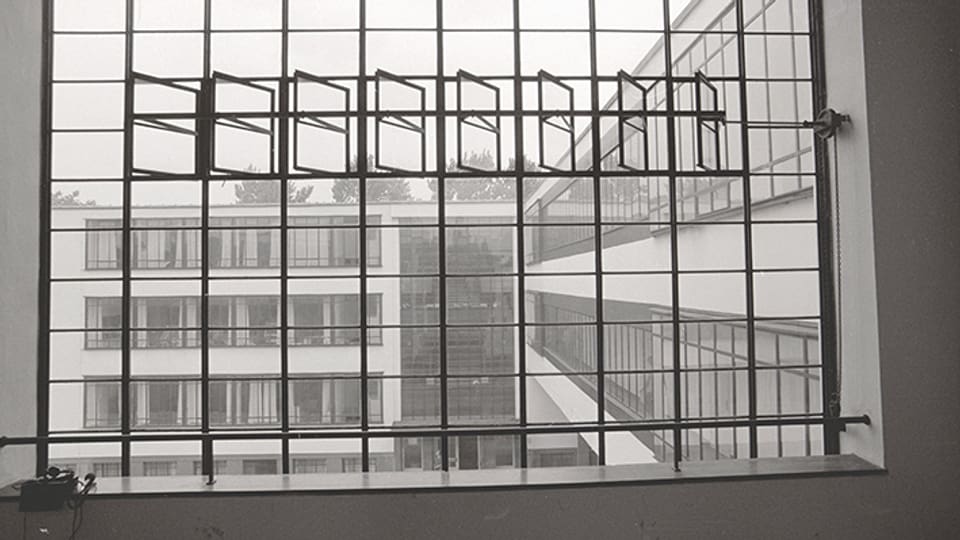 Blick durch ein Fenster mit zahkreichen Fensterkreuzen auf einen Gebäudekomplex.