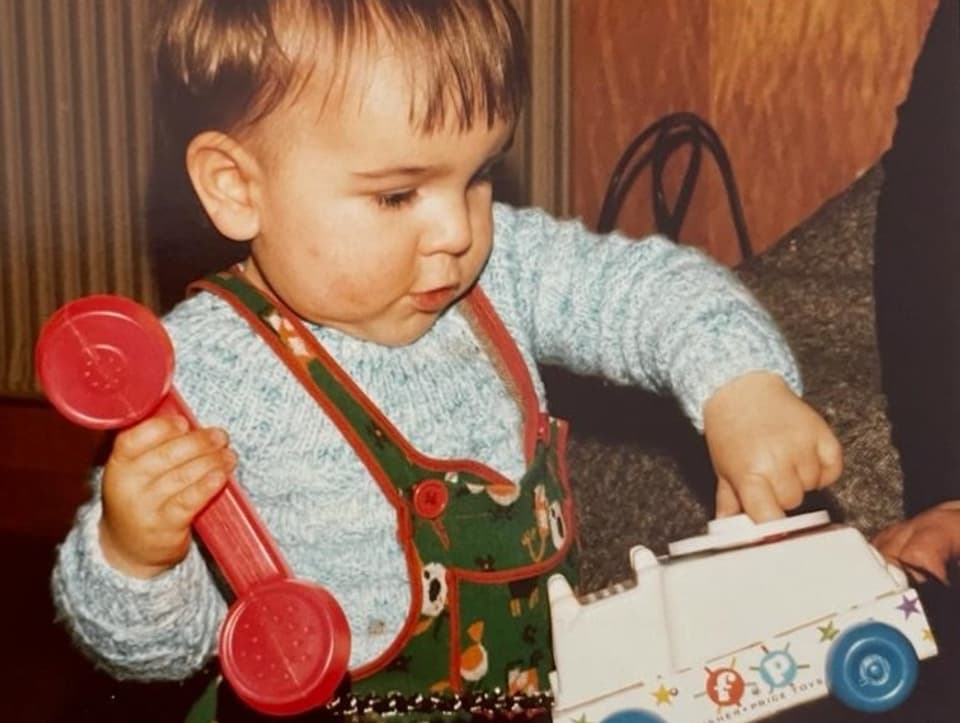 Magnus als Kleinkind mit einem Spielzeug-Telefon in der Hand und einem Spielzeugauto.