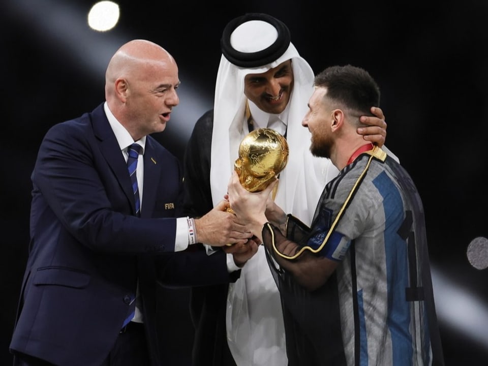 Gianni Infantino und Emir Tamim bin Hamad Al Thani herzen Lionel Messi, der einen Bischt trägt.